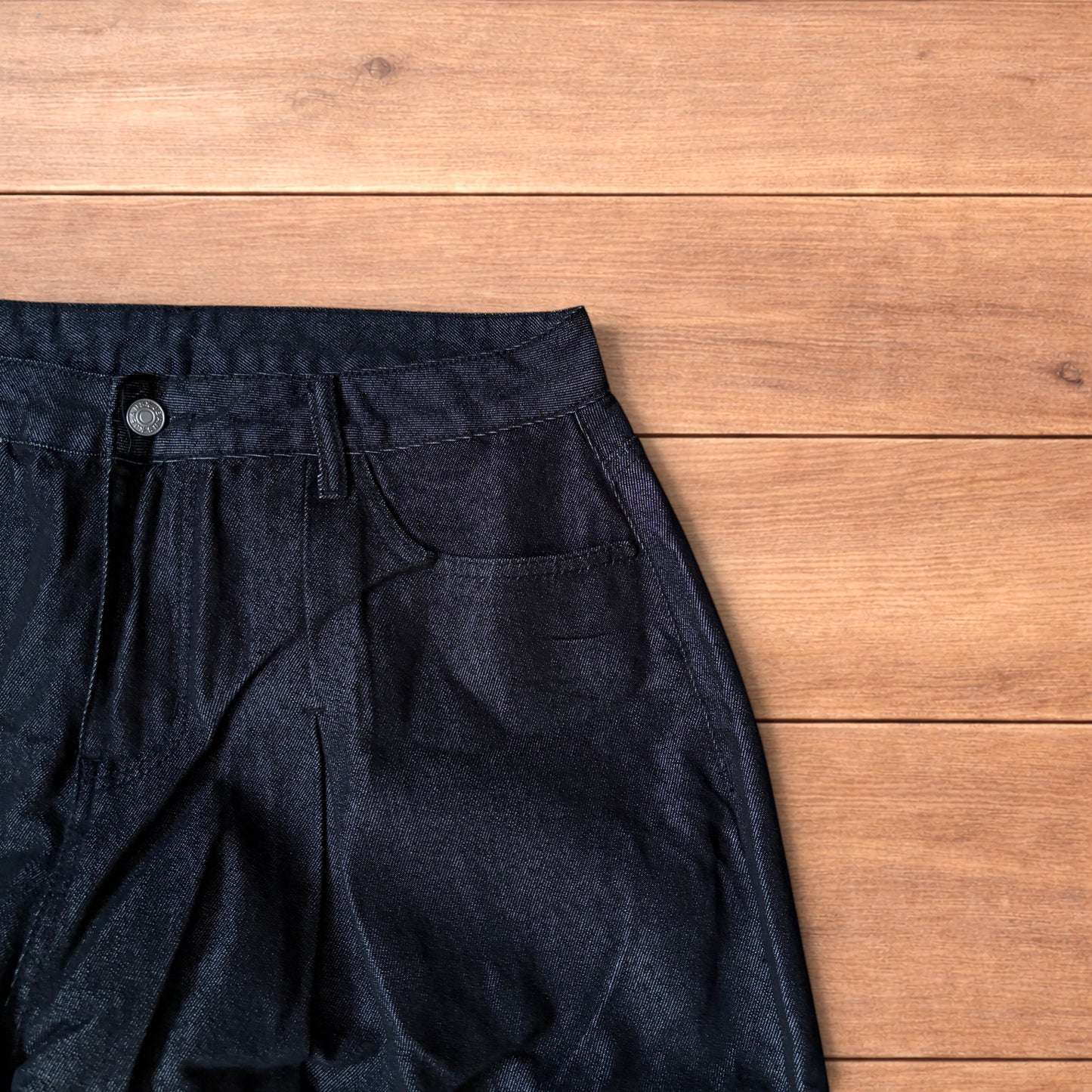 Dark grey baggy wide leg raw denim jeans laid flat showing front and back pockets and button fly