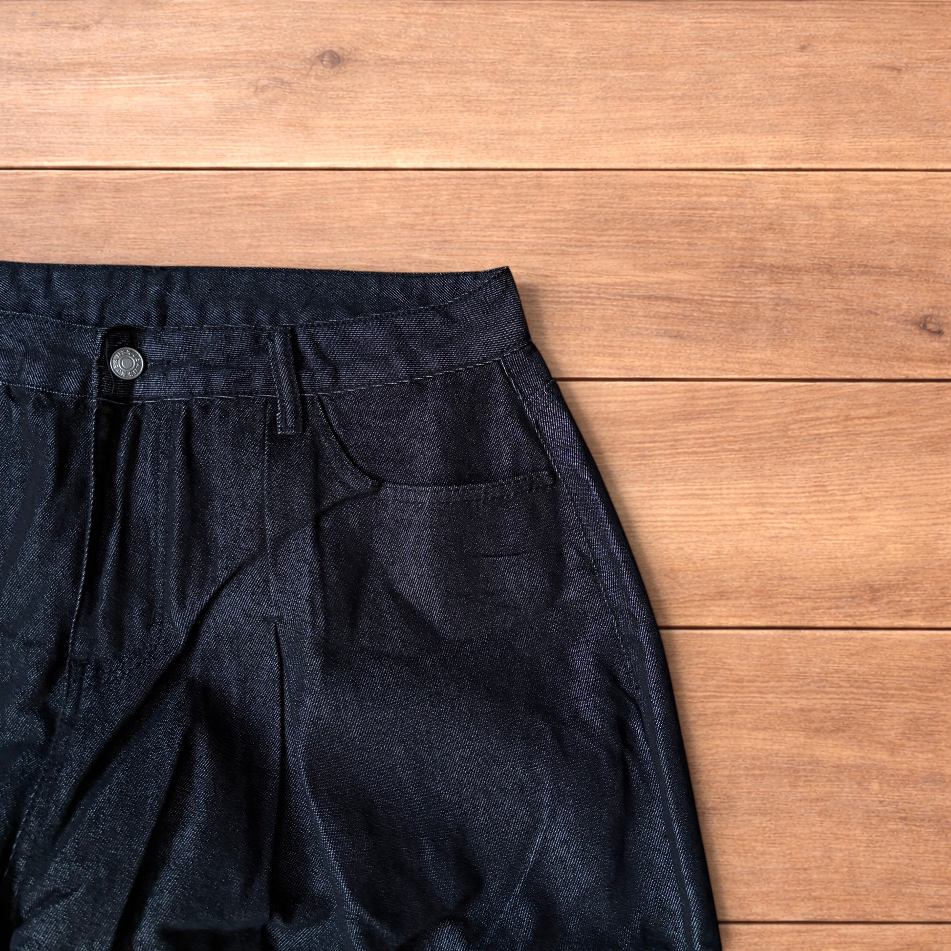 Dark grey baggy wide leg raw denim jeans laid flat showing front and back pockets and button fly