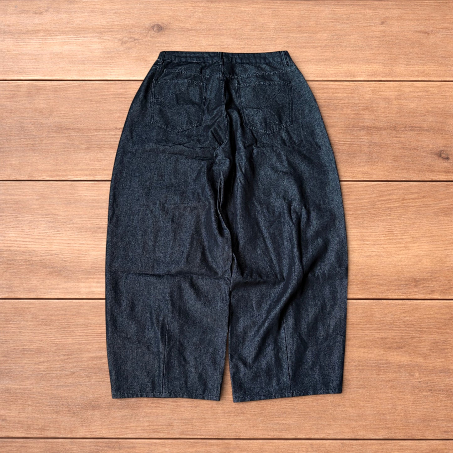 Dark grey baggy wide leg raw denim jeans laid flat showing front and back pockets and button fly