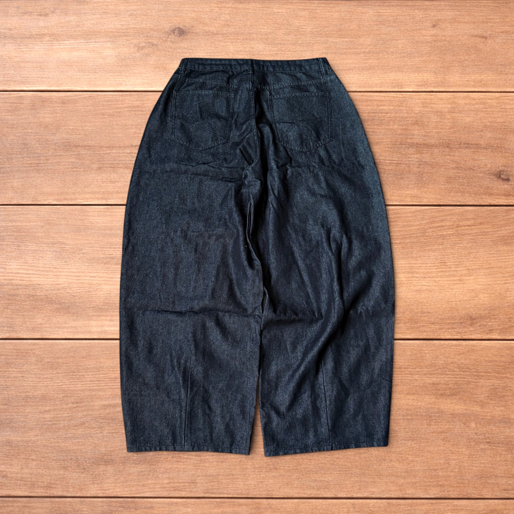 Dark grey baggy wide leg raw denim jeans laid flat showing front and back pockets and button fly