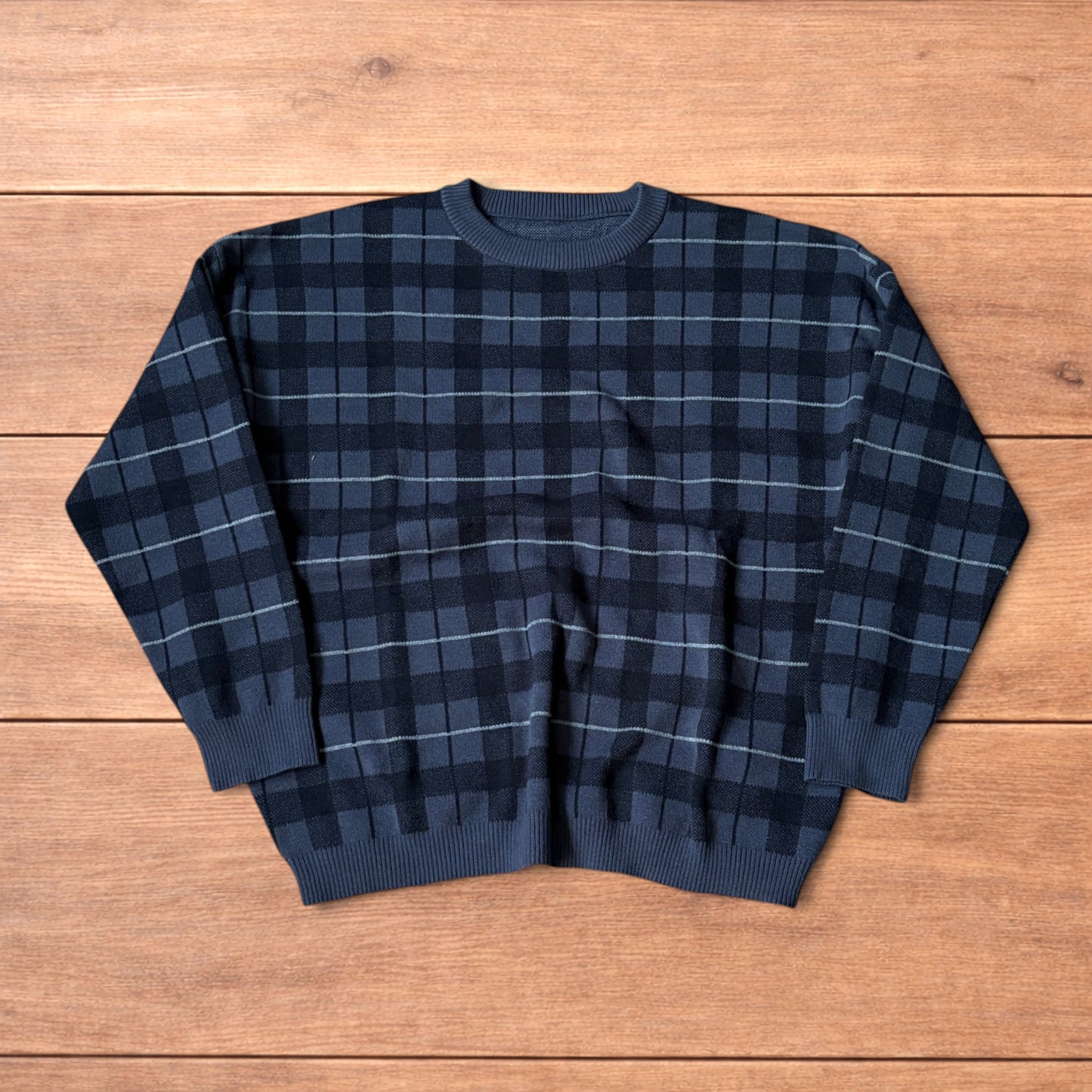 Vintage style checkered pullover jumper in grey black laid flat on wooden surface