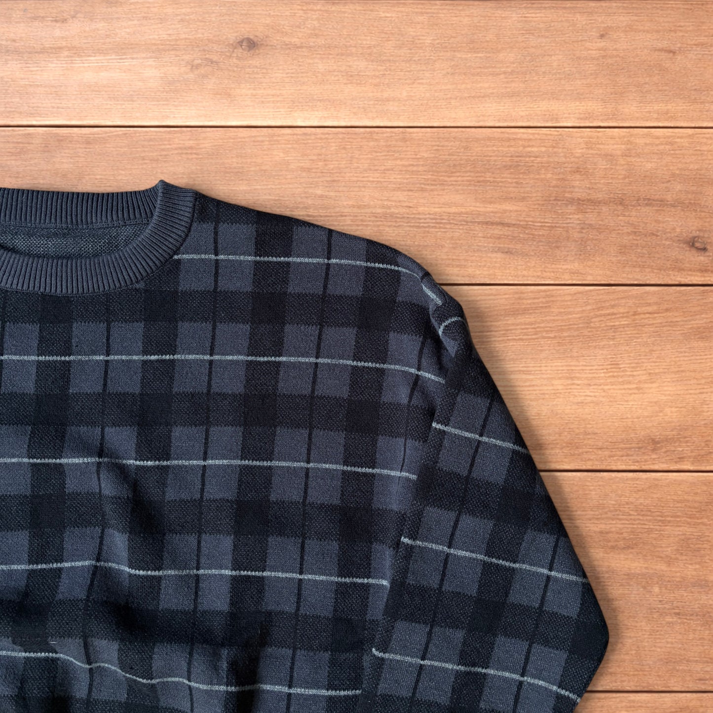 Vintage style checkered pullover jumper in grey black laid flat on wooden surface