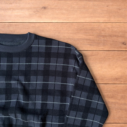 Vintage style checkered pullover jumper in grey black laid flat on wooden surface