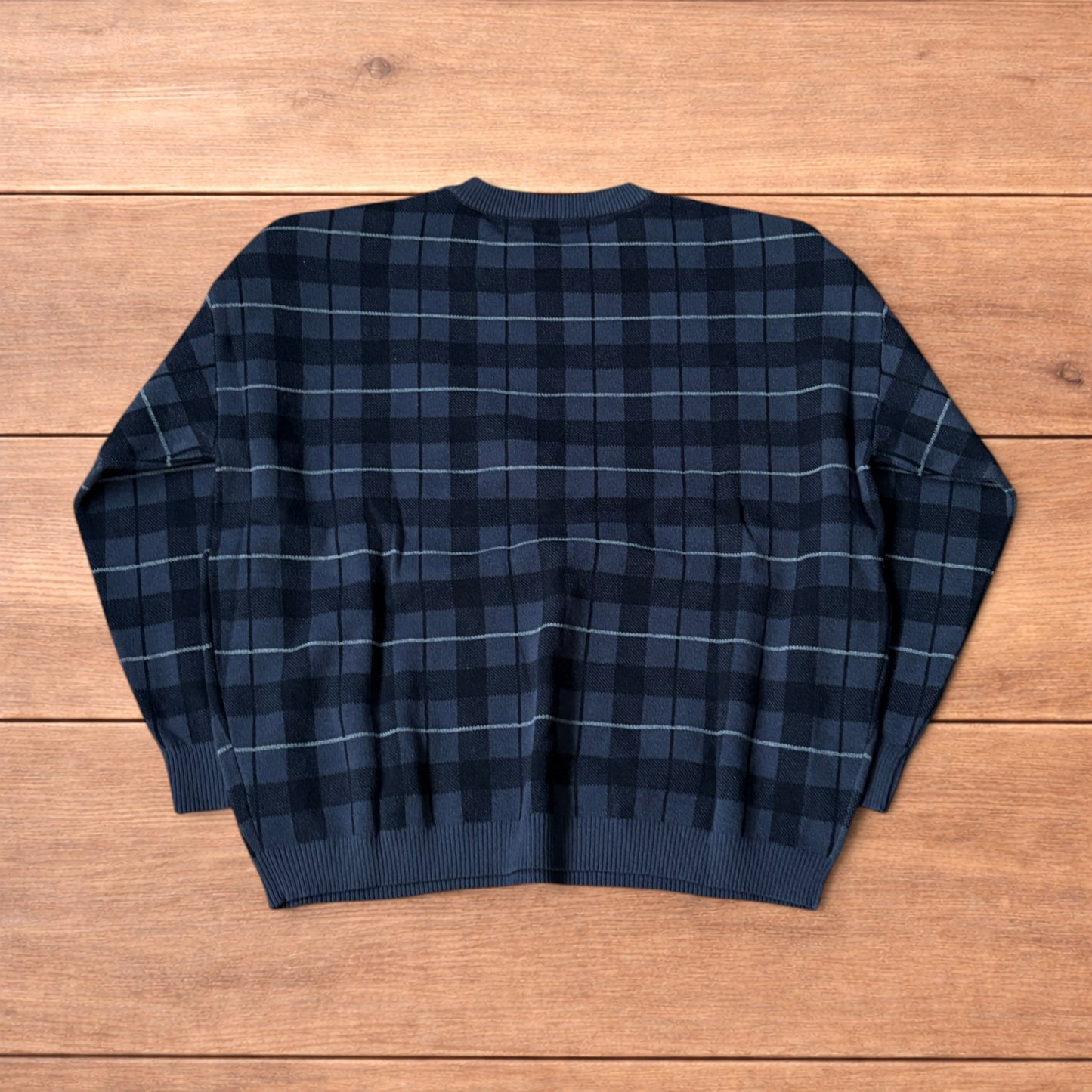 Vintage style checkered pullover jumper in grey black laid flat on wooden surface