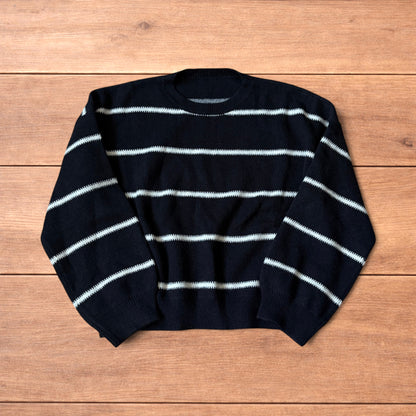 Black vintage style pullover jumper with white horizontal stripes laid flat on wood surface.