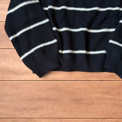 Black vintage style pullover jumper with white horizontal stripes laid flat on wood surface.