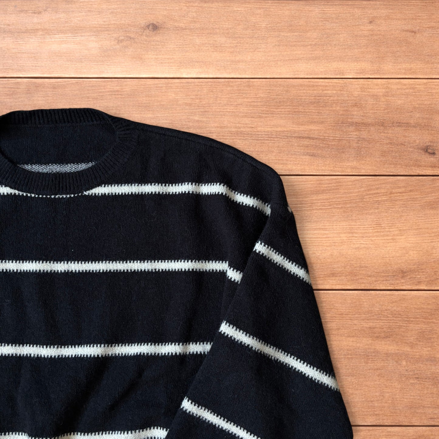 Black vintage style pullover jumper with white horizontal stripes laid flat on wood surface.