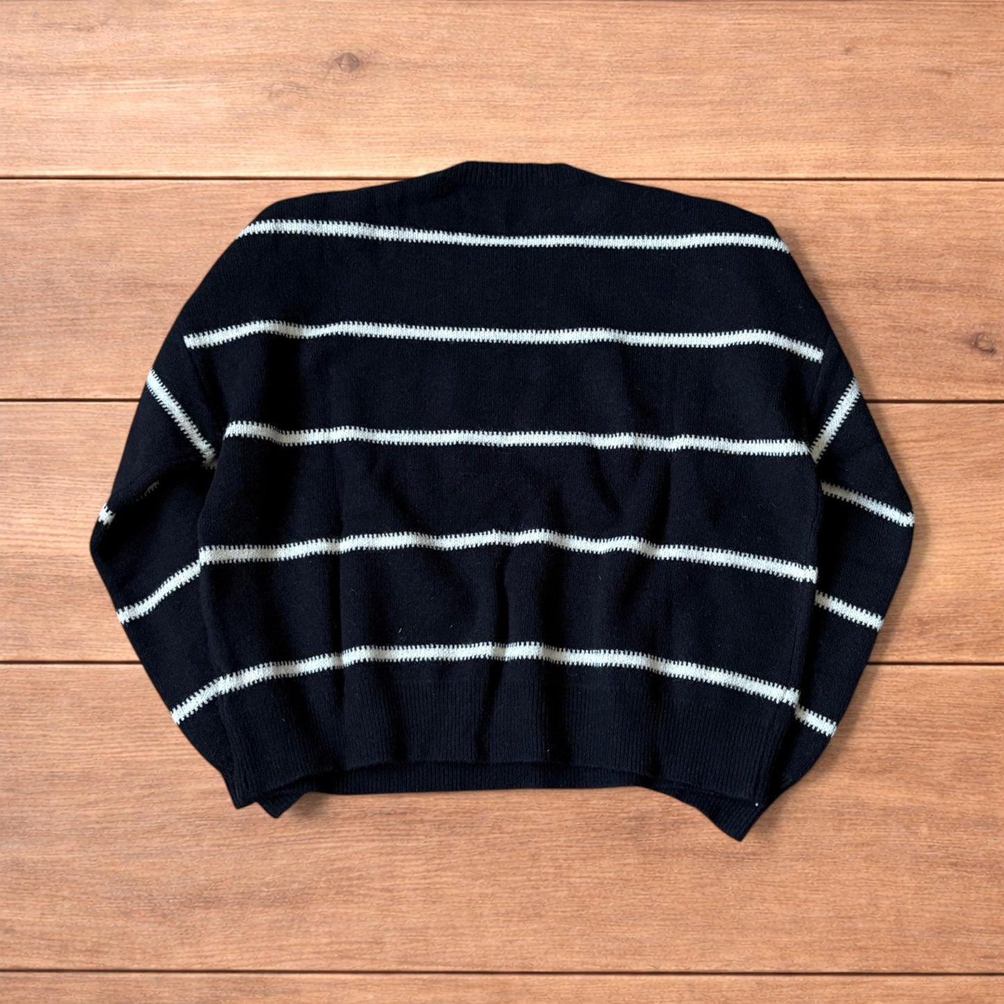 Black vintage style pullover jumper with white horizontal stripes laid flat on wood surface.