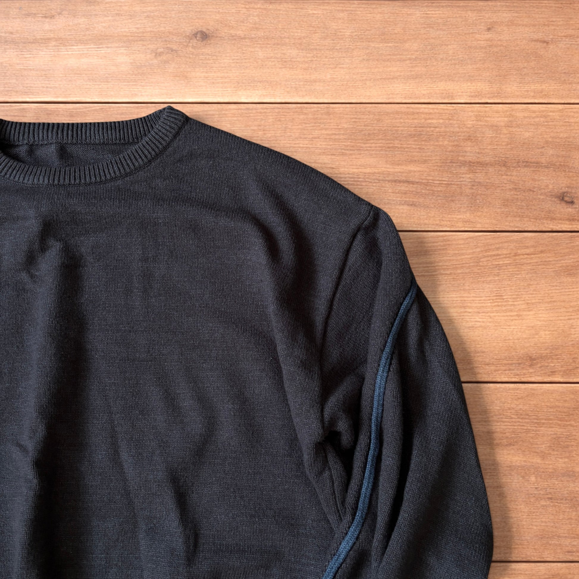 Dark grey vintage style pullover jumper with slim blue piping detail on sleeves laid flat on wooden surface.