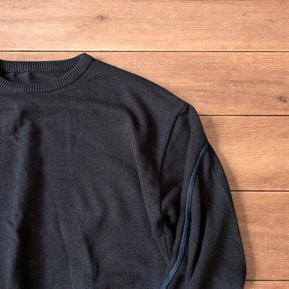 Dark grey vintage style pullover jumper with slim blue piping detail on sleeves laid flat on wooden surface.