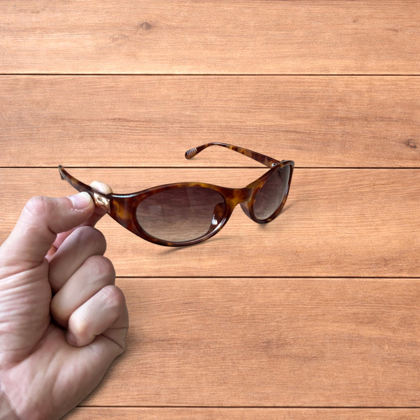 Vintage style tortoiseshell sunglasses with brown lenses held against a wooden background.