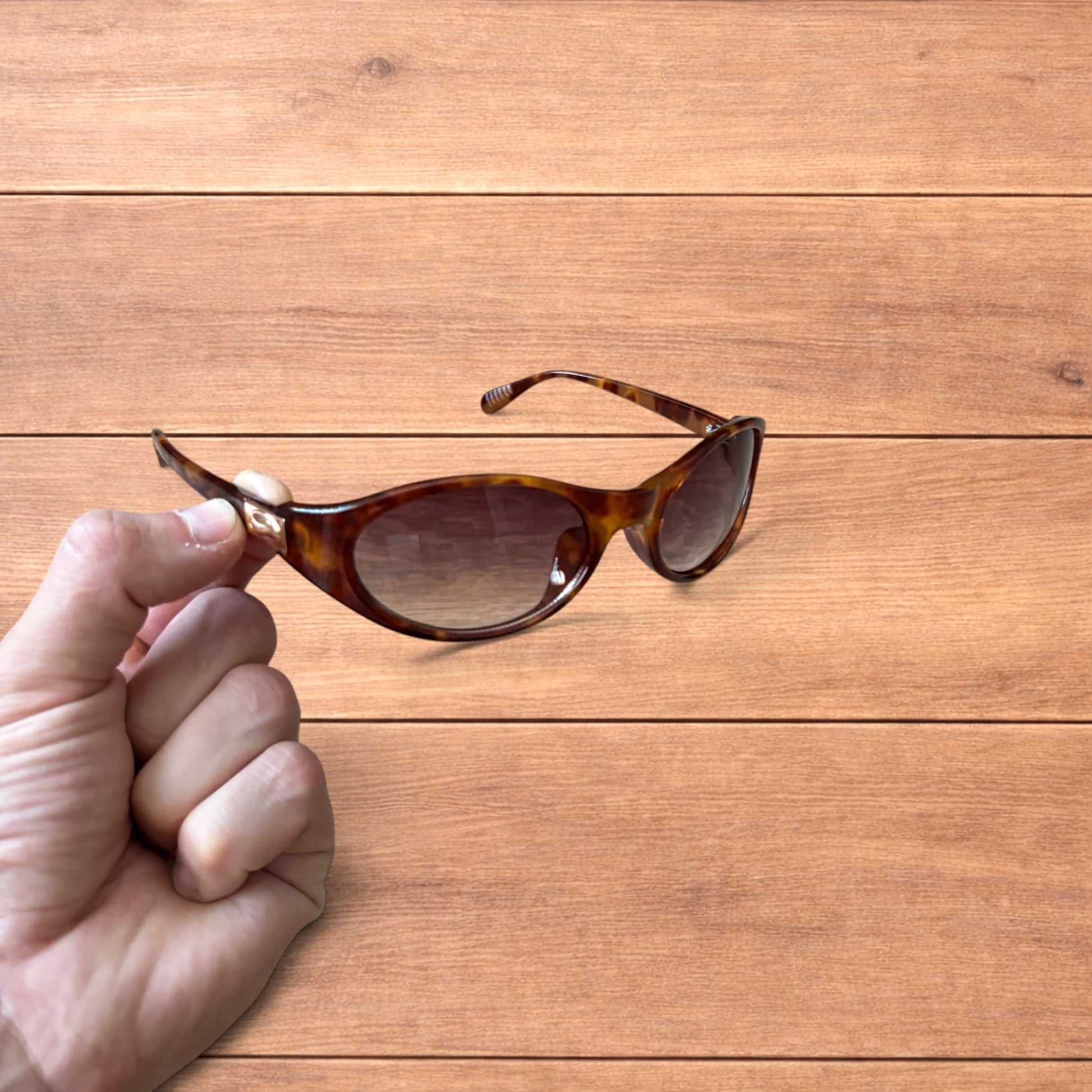Vintage style tortoiseshell sunglasses with brown lenses held against a wooden background.
