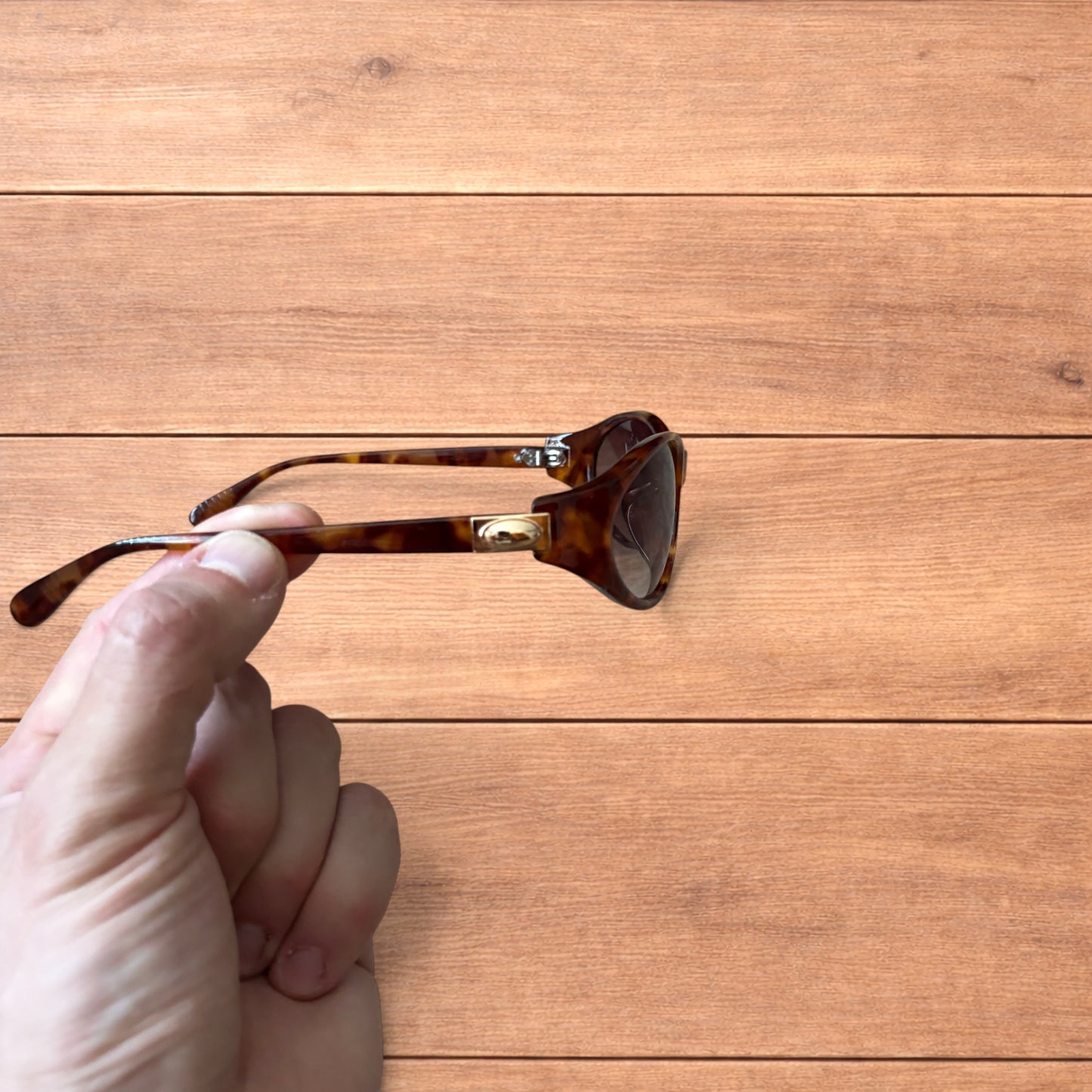 Vintage style tortoiseshell sunglasses with brown lenses held against a wooden background.