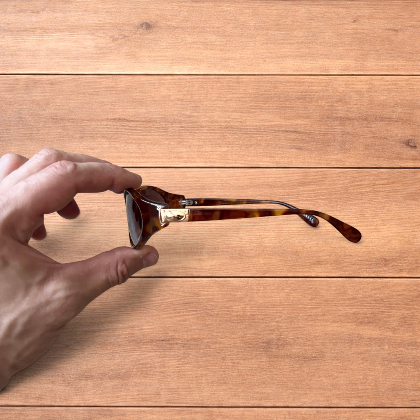Vintage style tortoiseshell sunglasses with brown lenses held against a wooden background.