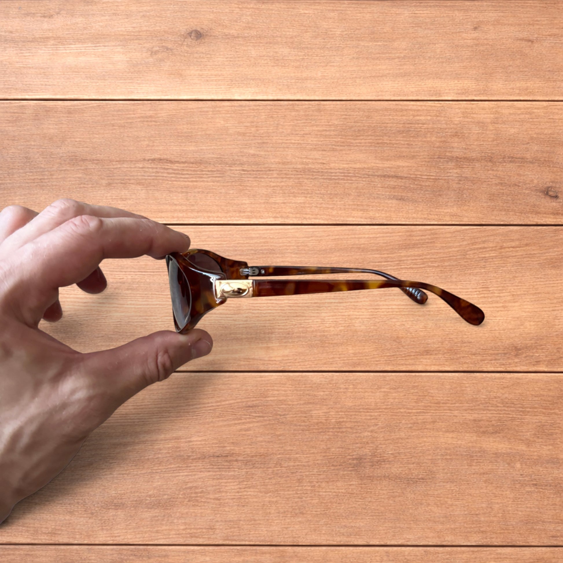Vintage style tortoiseshell sunglasses with brown lenses held against a wooden background.