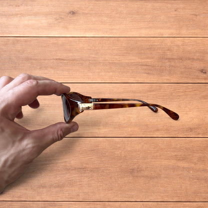 Vintage style tortoiseshell sunglasses with brown lenses held against a wooden background.
