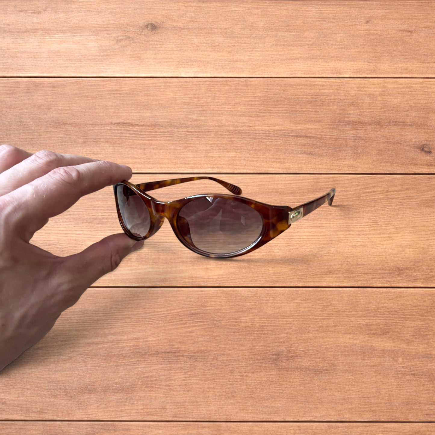 Vintage style tortoiseshell sunglasses with brown lenses held against a wooden background.
