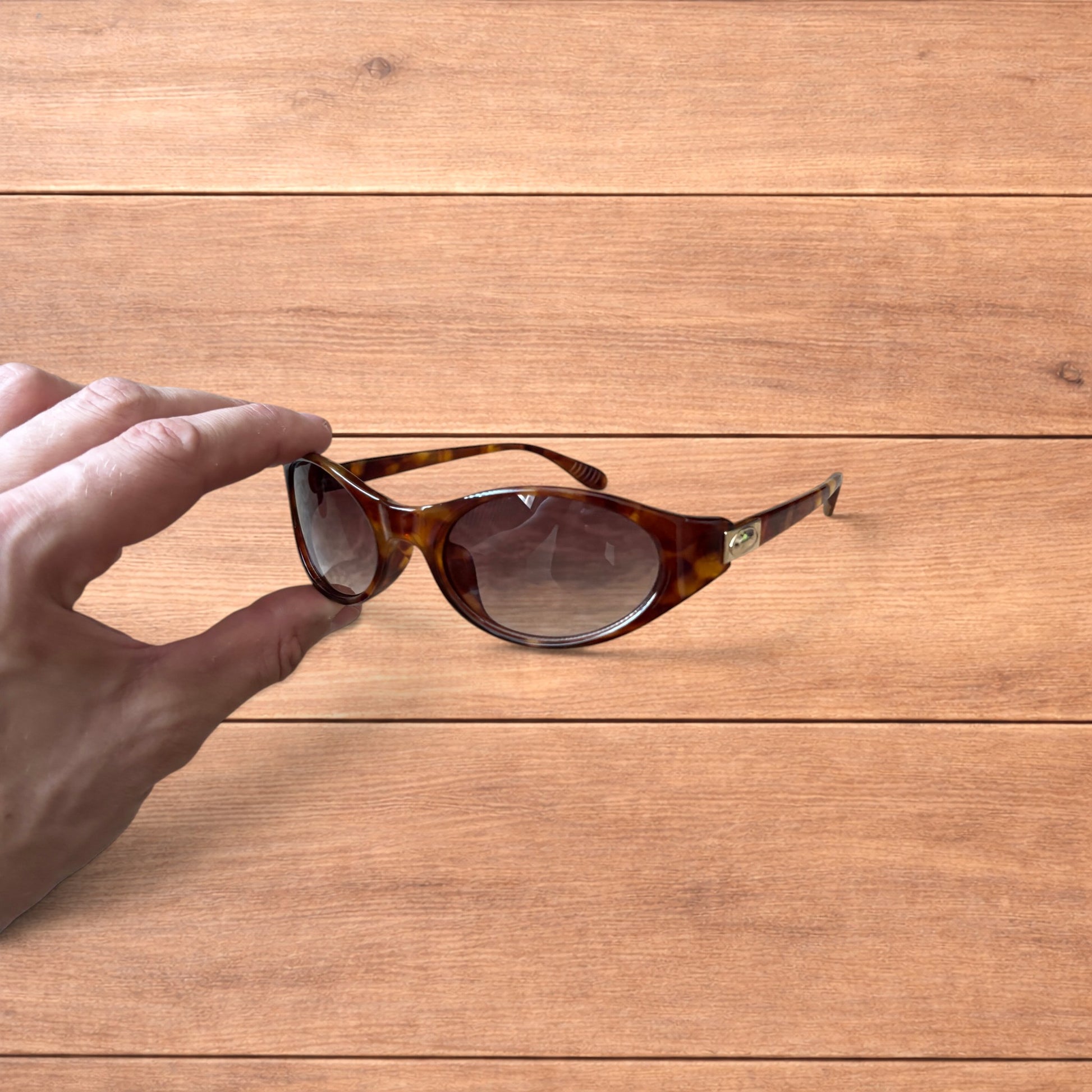 Vintage style tortoiseshell sunglasses with brown lenses held against a wooden background.