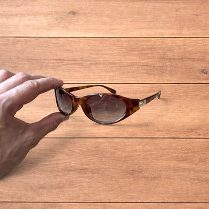 Vintage style tortoiseshell sunglasses with brown lenses held against a wooden background.