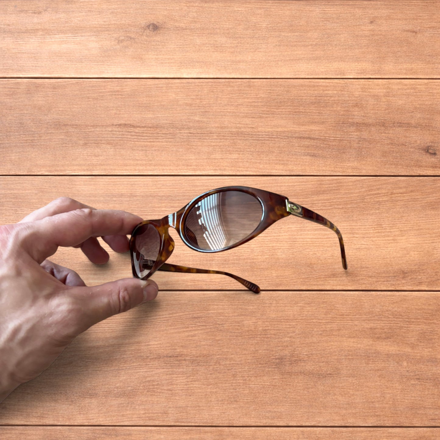 Vintage style tortoiseshell sunglasses with brown lenses held against a wooden background.