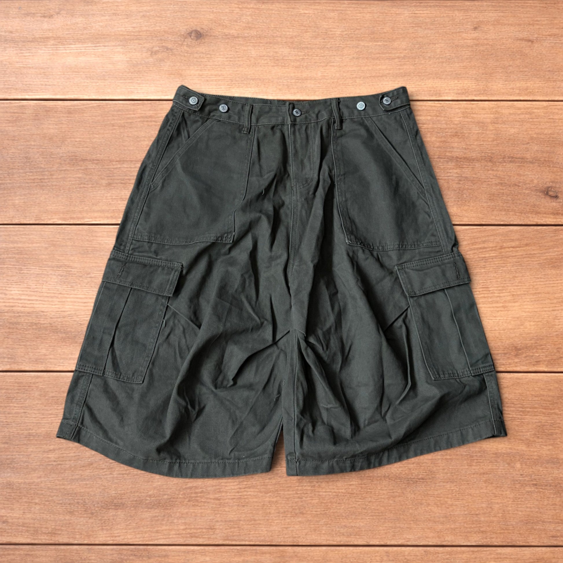 Vintage style baggy cargo shorts in khaki green laid flat on wooden surface showing front and back details.