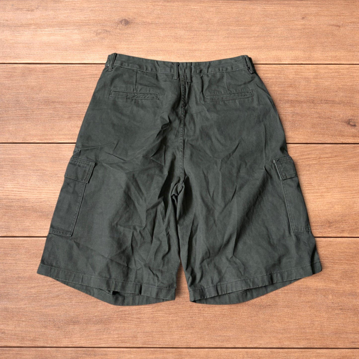 Vintage style baggy cargo shorts in khaki green laid flat on wooden surface showing front and back details.