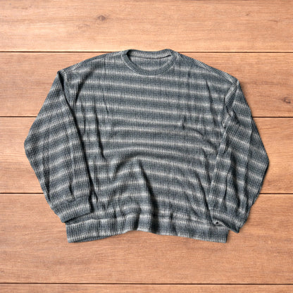 Vintage style striped knitted sweater jumper in grey and beige laid flat on wooden surface, showing ribbed texture and crew neck.