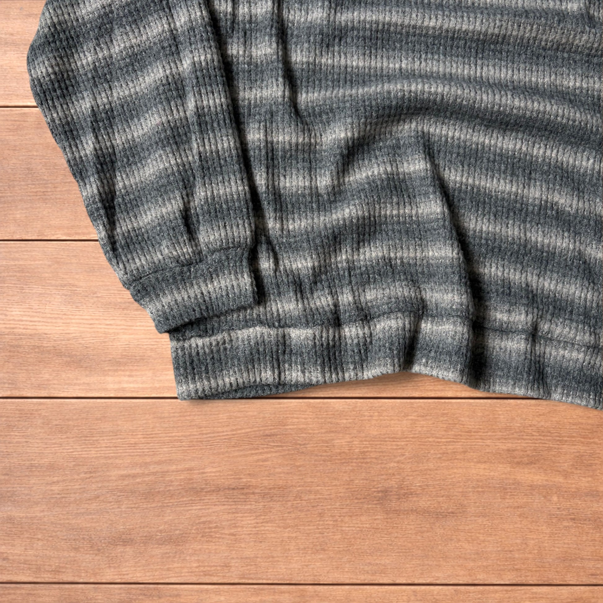 Vintage style striped knitted sweater jumper in grey and beige laid flat on wooden surface, showing ribbed texture and crew neck.