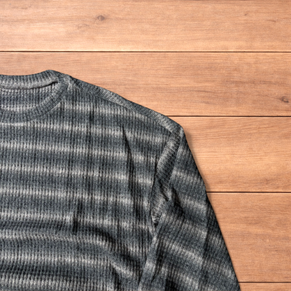 Vintage style striped knitted sweater jumper in grey and beige laid flat on wooden surface, showing ribbed texture and crew neck.