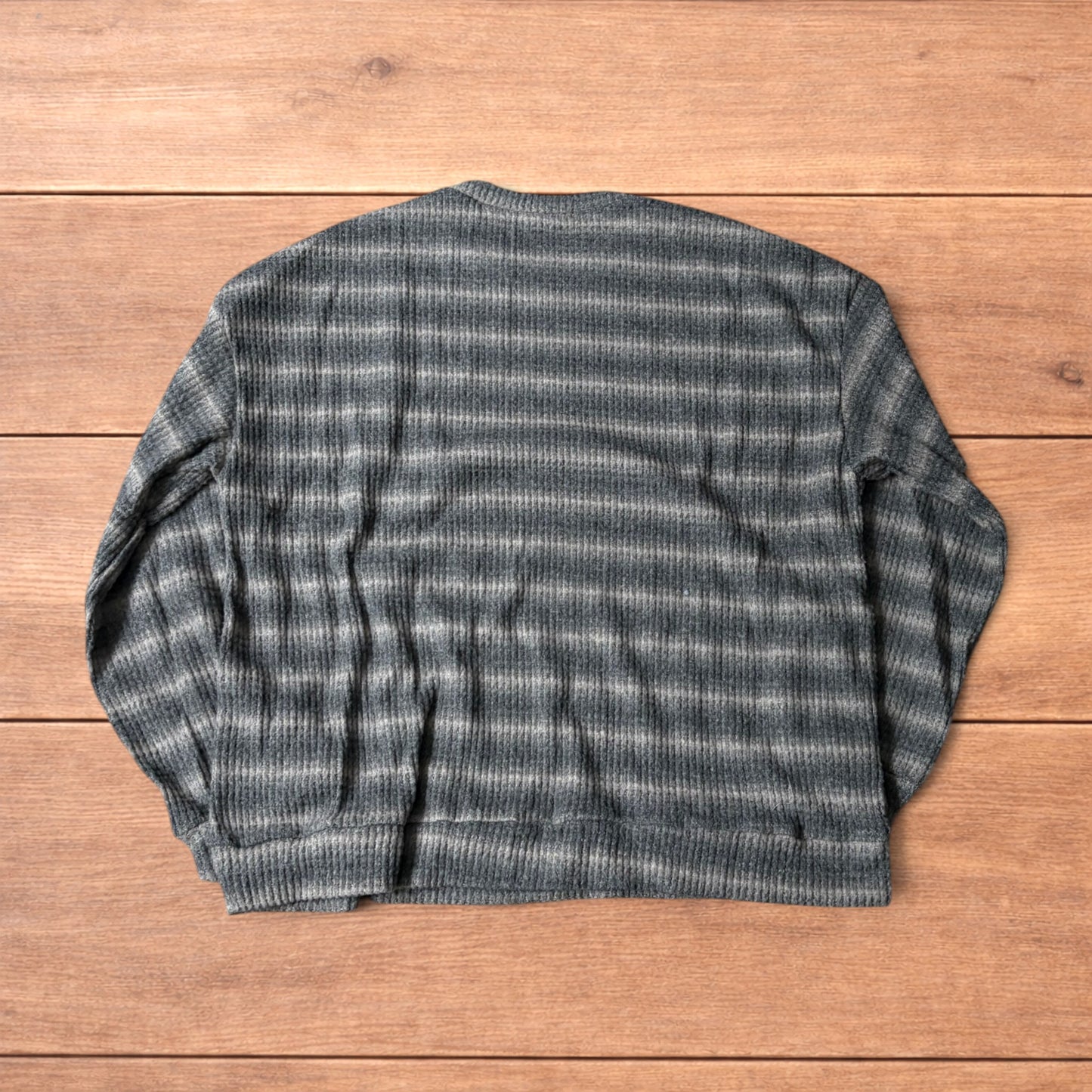 Vintage style striped knitted sweater jumper in grey and beige laid flat on wooden surface, showing ribbed texture and crew neck.