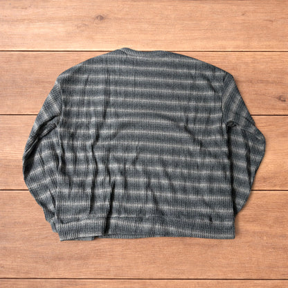 Vintage style striped knitted sweater jumper in grey and beige laid flat on wooden surface, showing ribbed texture and crew neck.
