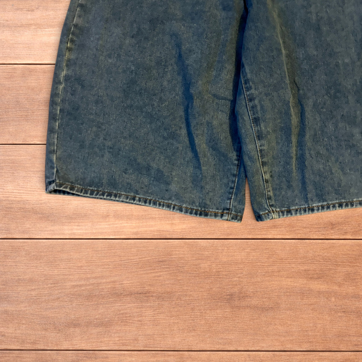 Mid blue baggy wide leg denim jorts shorts with front and back pockets laid flat on wooden background.