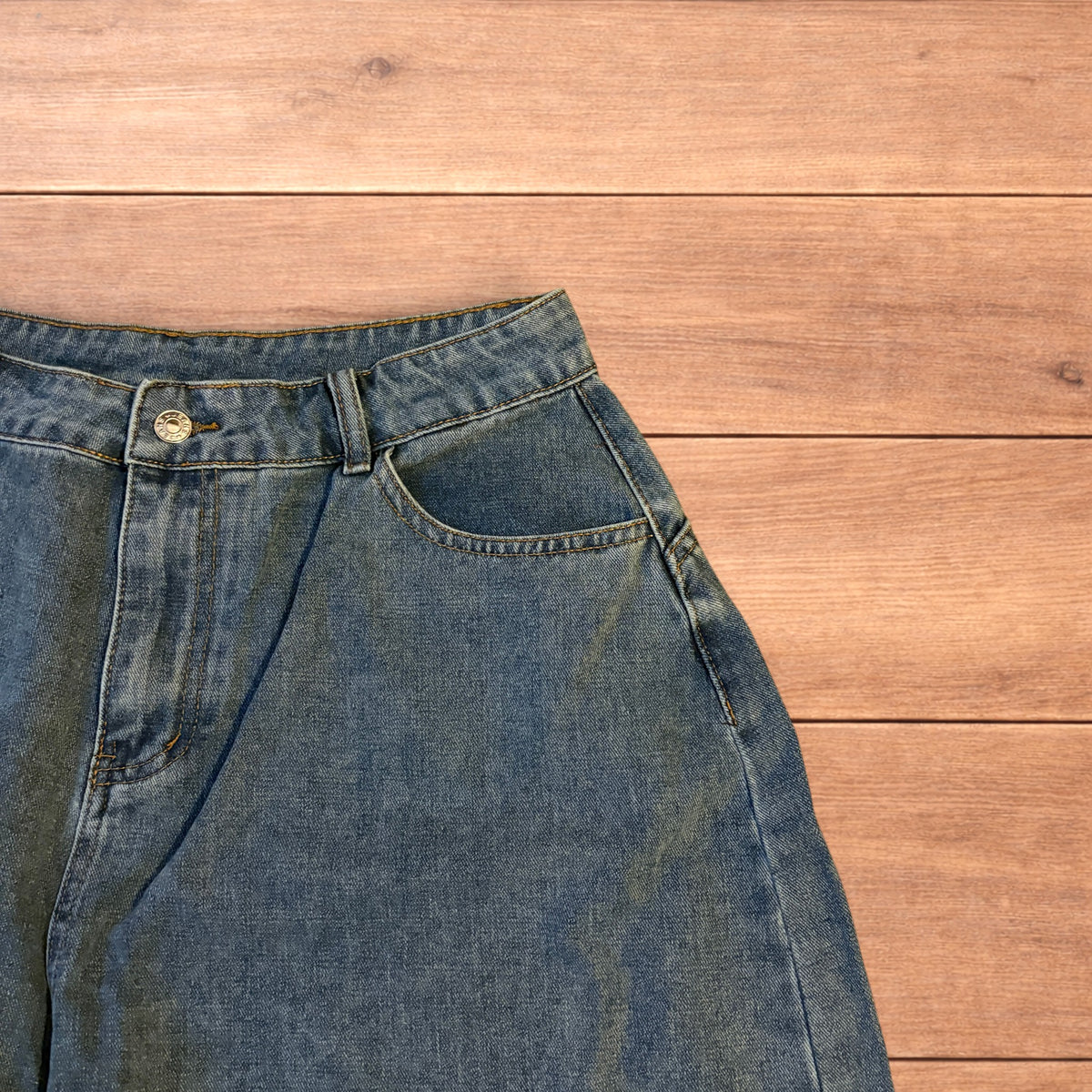 Mid blue baggy wide leg denim jorts shorts with front and back pockets laid flat on wooden background.