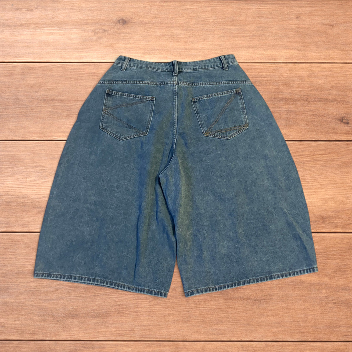 Mid blue baggy wide leg denim jorts shorts with front and back pockets laid flat on wooden background.