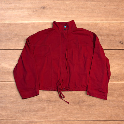 Red vintage style cropped zip up track jacket with high neck and drawstring waist laid flat on wooden surface.