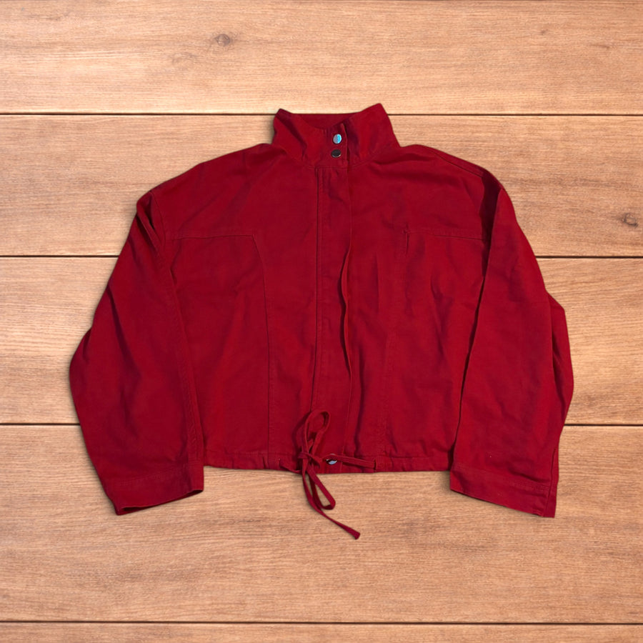 Red vintage style cropped zip up track jacket with high neck and drawstring waist laid flat on wooden surface.