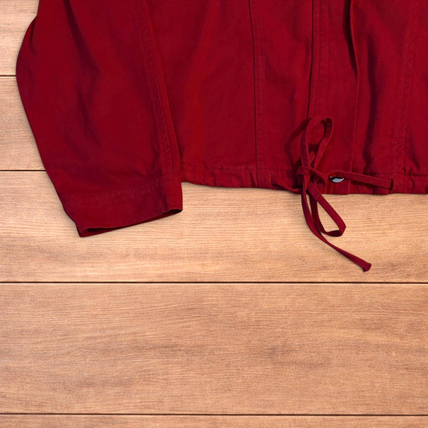 Red vintage style cropped zip up track jacket with high neck and drawstring waist laid flat on wooden surface.