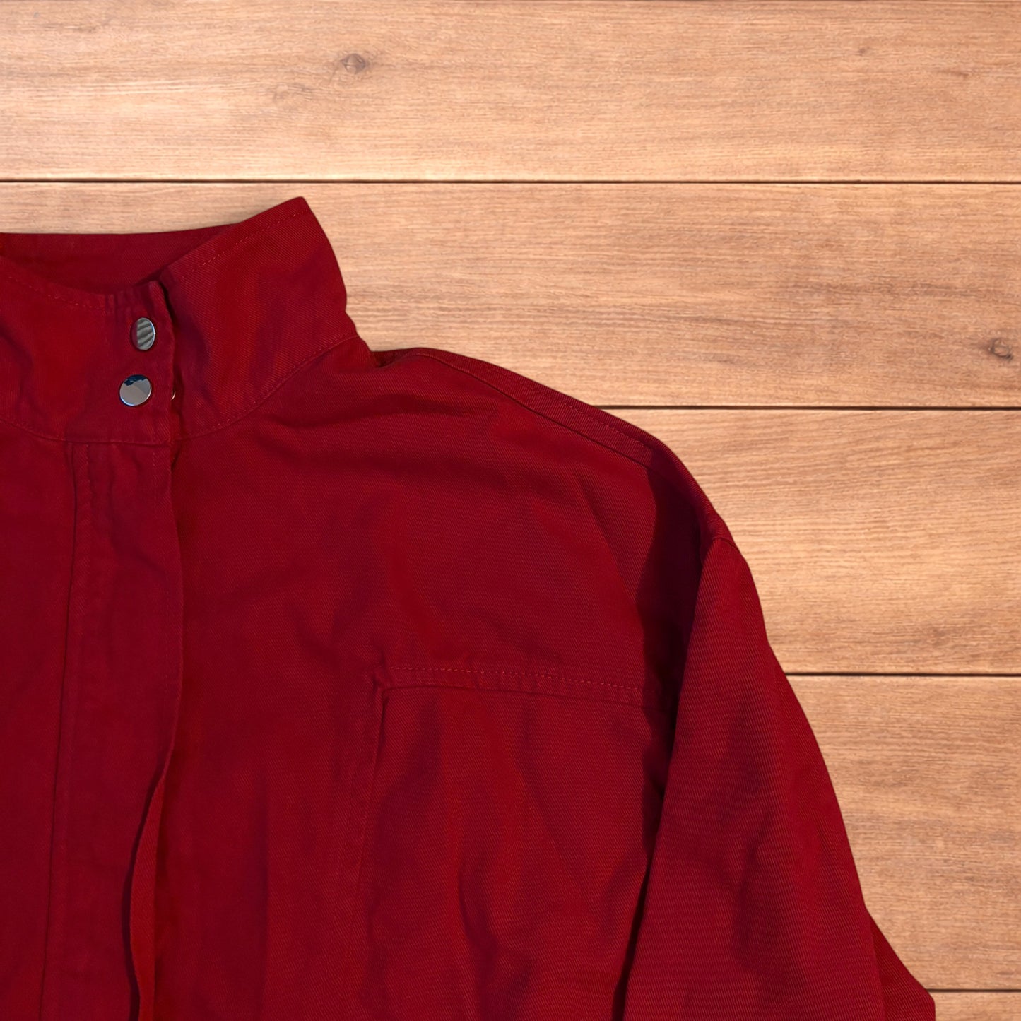 Red vintage style cropped zip up track jacket with high neck and drawstring waist laid flat on wooden surface.