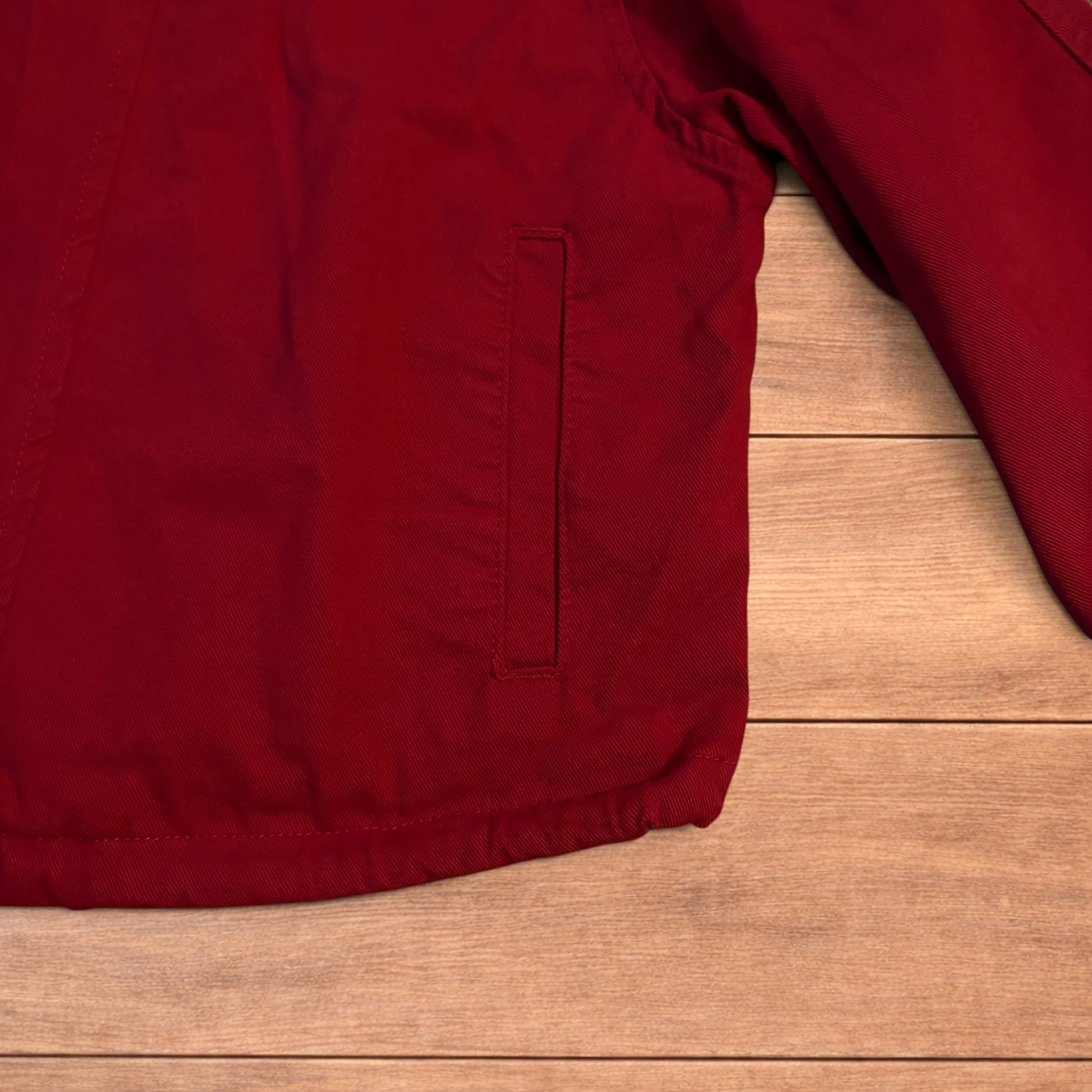 Red vintage style cropped zip up track jacket with high neck and drawstring waist laid flat on wooden surface.