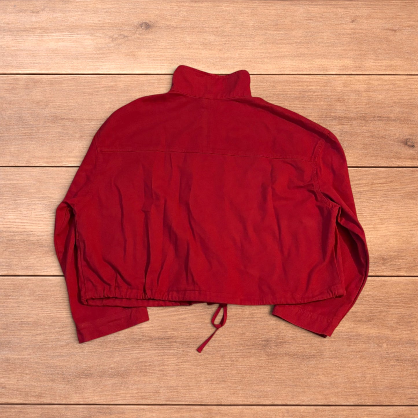Red vintage style cropped zip up track jacket with high neck and drawstring waist laid flat on wooden surface.
