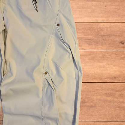 Beige baggy gorpcore hiking pants laid flat showing drawstring waist, toggled hems and back flap pockets.