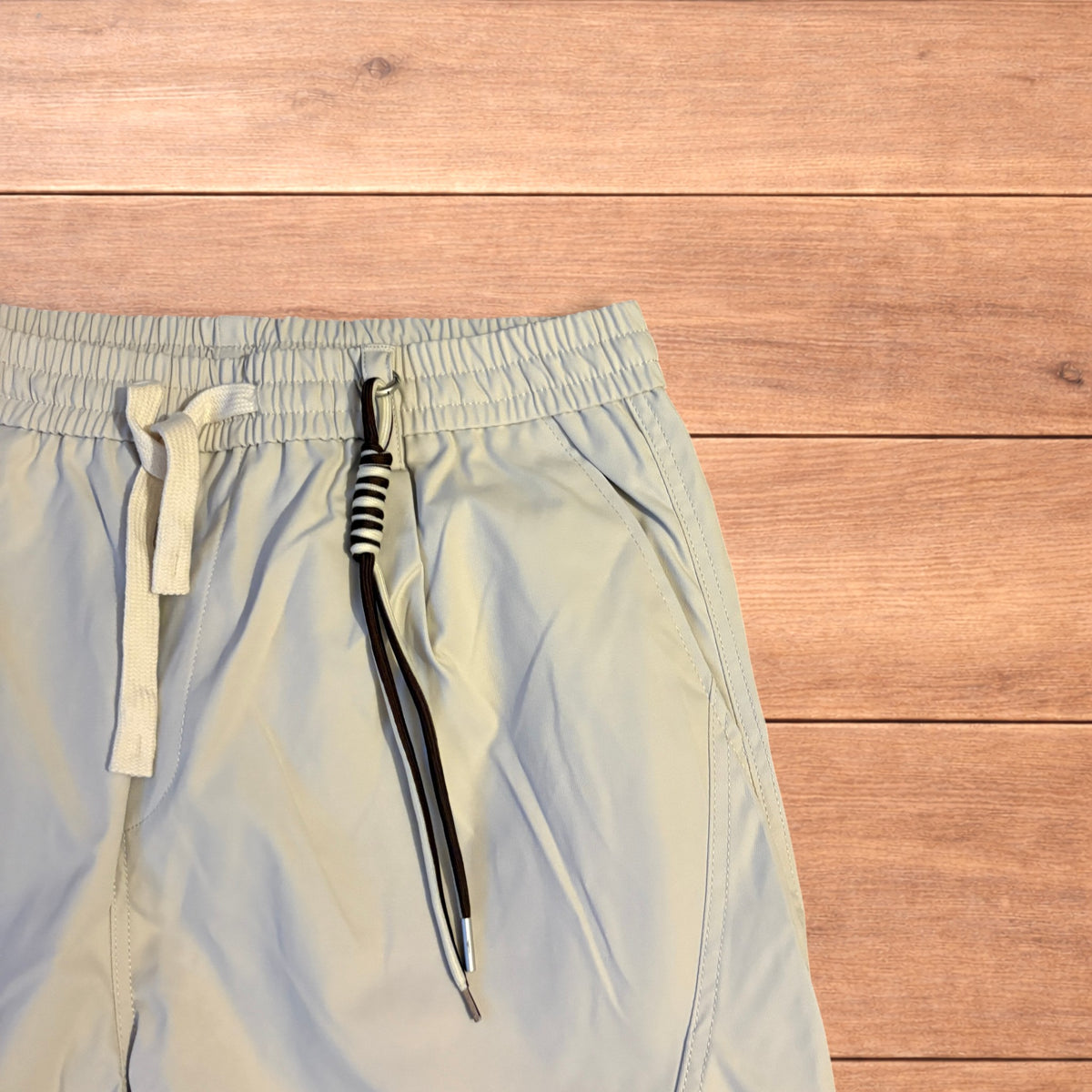 Beige baggy gorpcore hiking pants laid flat showing drawstring waist, toggled hems and back flap pockets.