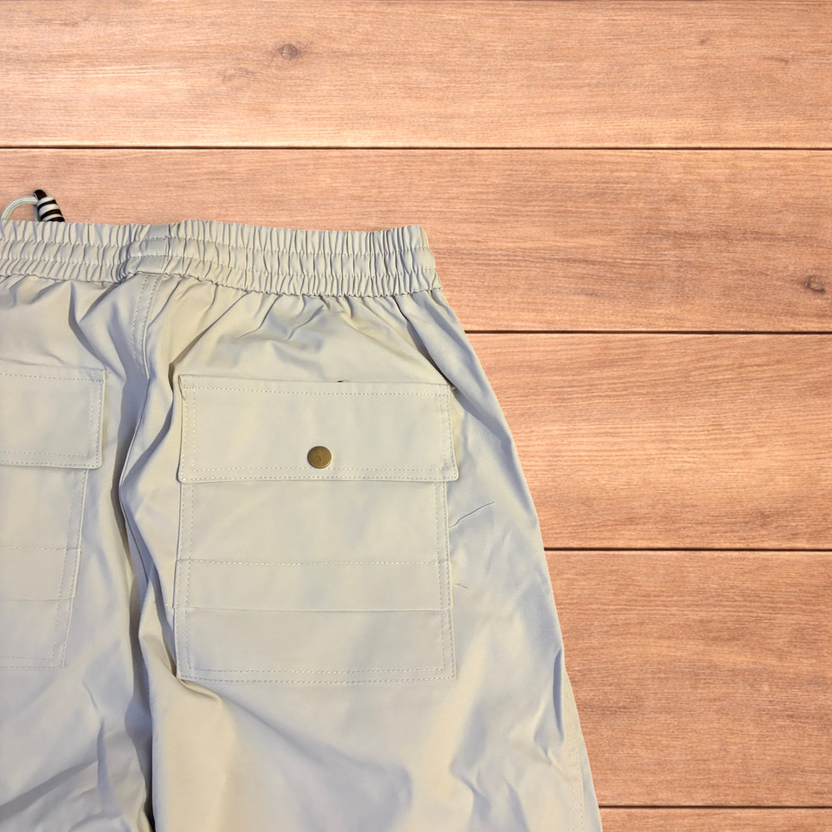 Beige baggy gorpcore hiking pants laid flat showing drawstring waist, toggled hems and back flap pockets.