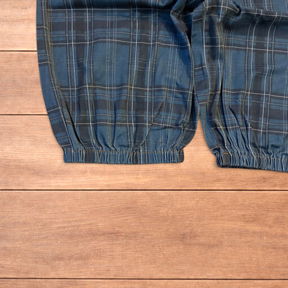 Baggy wide leg checkered navy blue parachute jogger trousers laid flat on a wooden surface