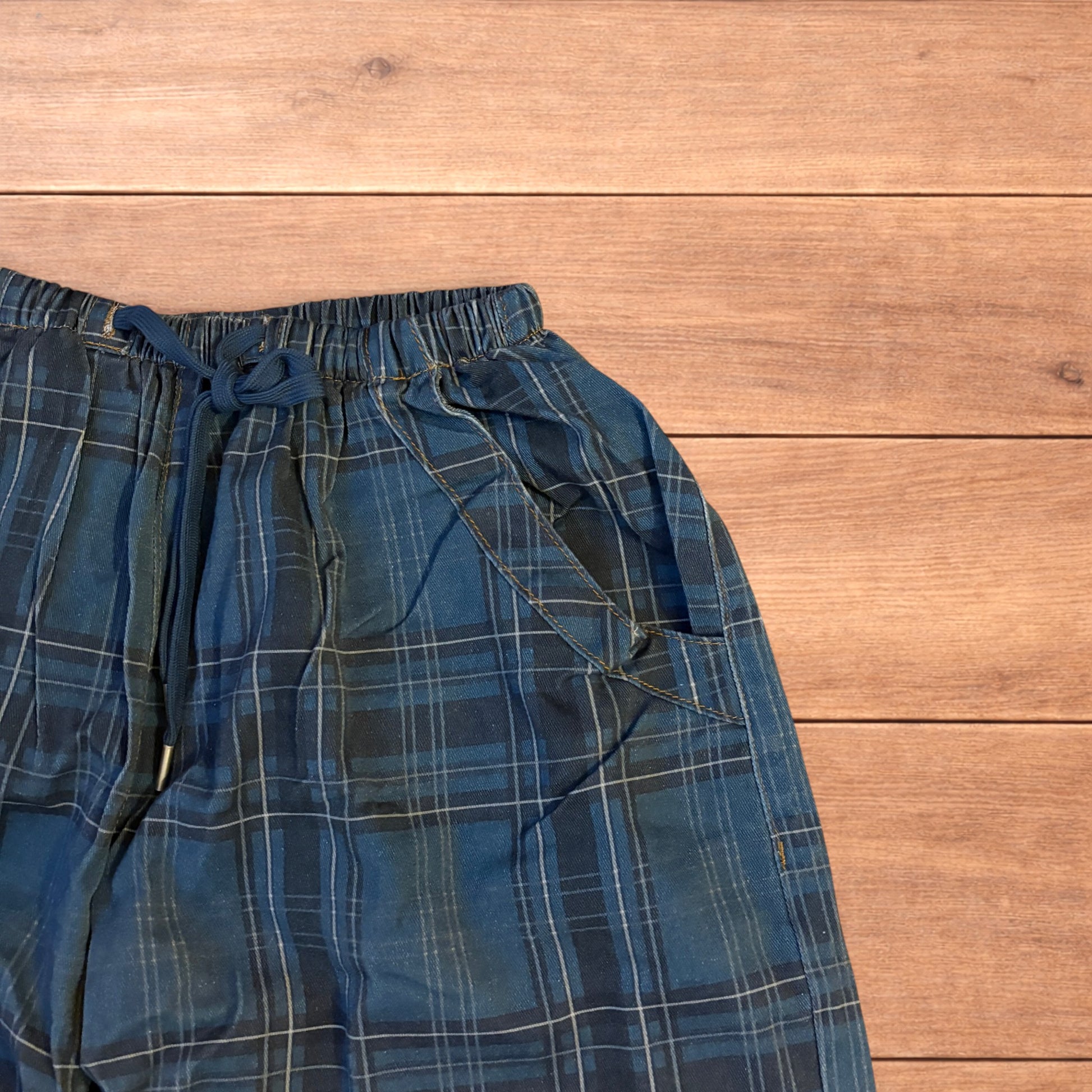 Baggy wide leg checkered navy blue parachute jogger trousers laid flat on a wooden surface