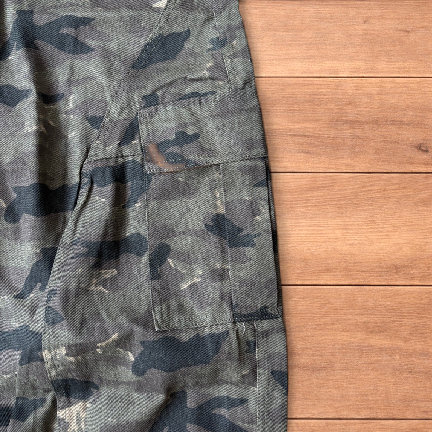 Baggy wide leg cargo trousers in army camo laid flat showing front, back and close-up details on wooden background.