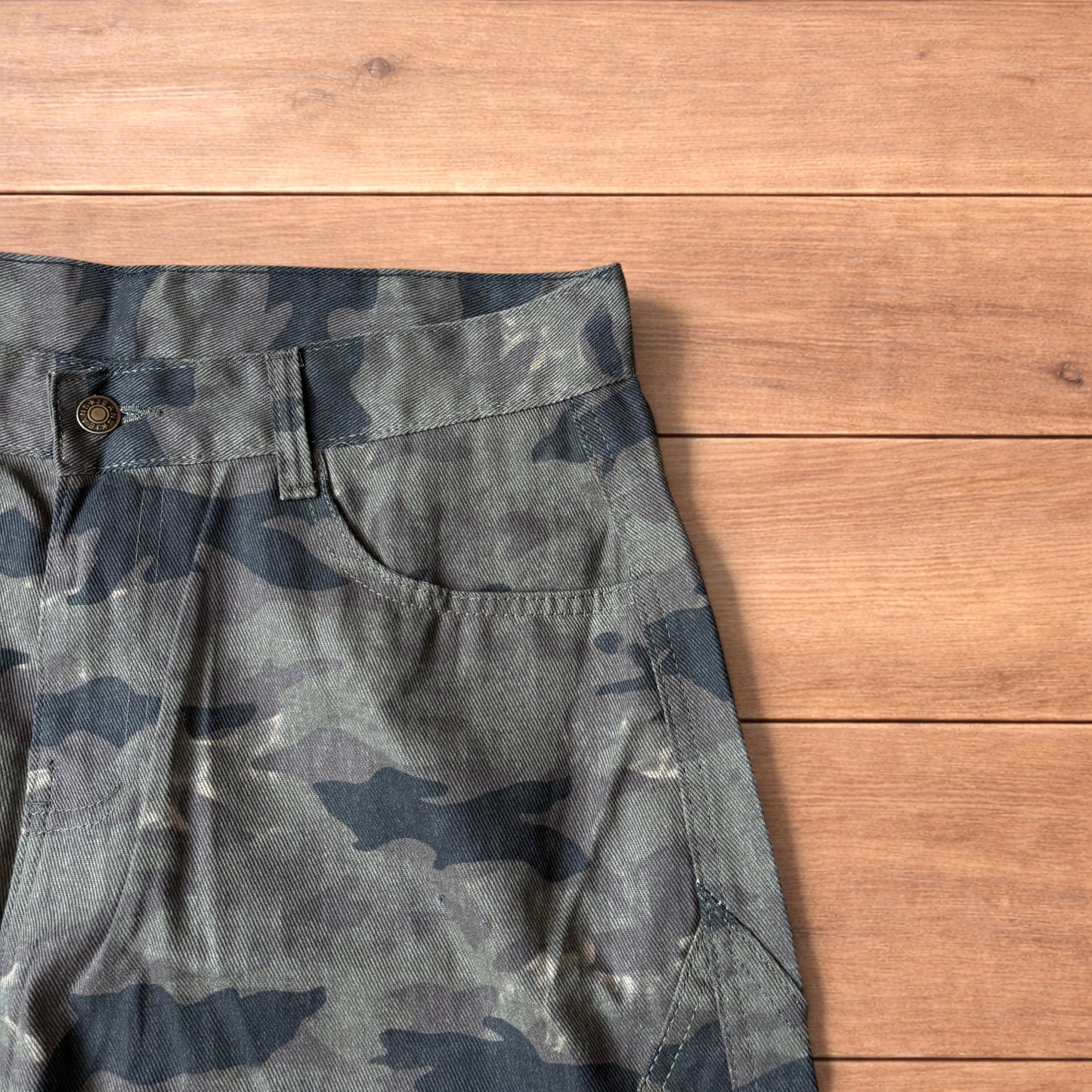 Baggy wide leg cargo trousers in army camo laid flat showing front, back and close-up details on wooden background.