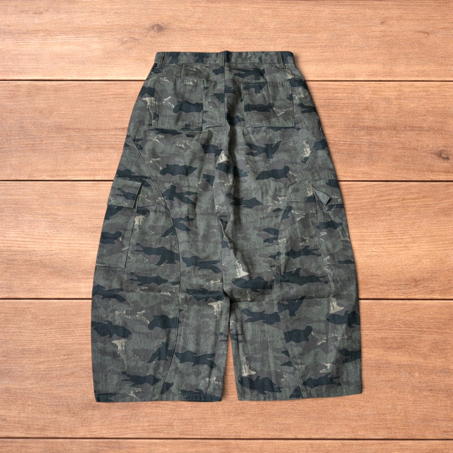 Baggy wide leg cargo trousers in army camo laid flat showing front, back and close-up details on wooden background.