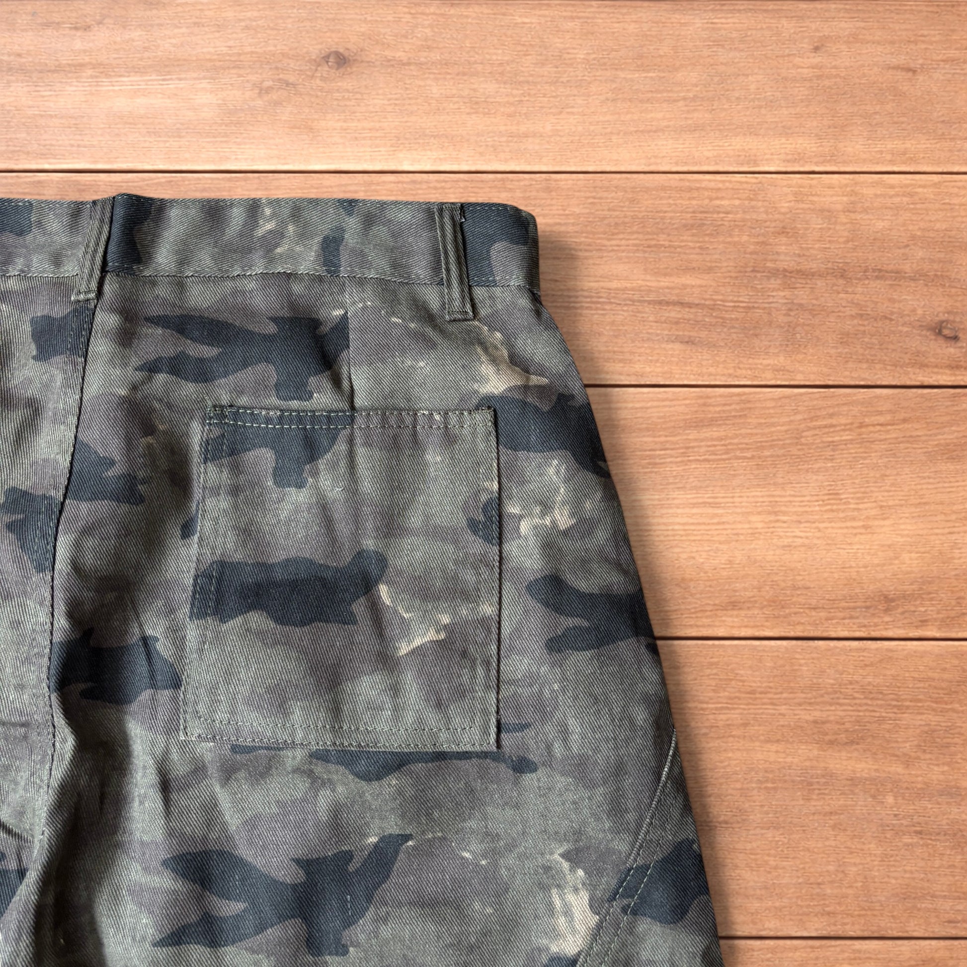 Baggy wide leg cargo trousers in army camo laid flat showing front, back and close-up details on wooden background.