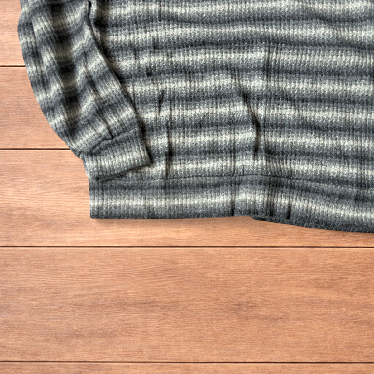 Vintage style knitted sweater jumper with khaki and beige stripes laid flat on wooden surface.